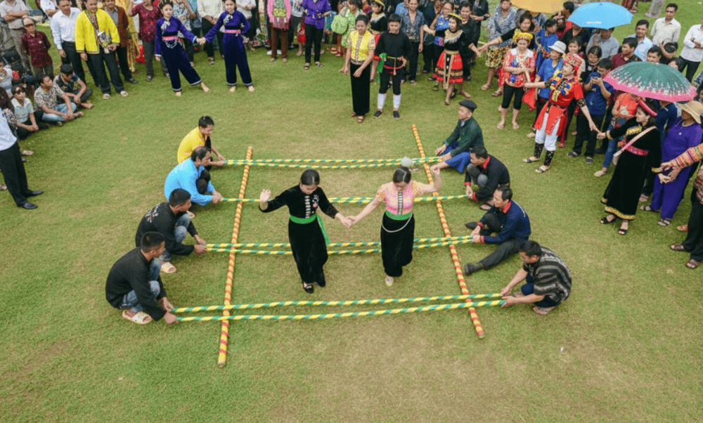 Dancers hop and weave between clapping bamboo poles that are rhythmically tapped by others on the ground
